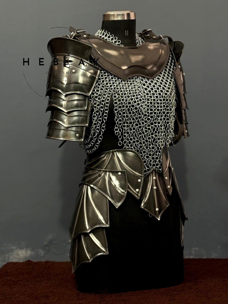 May include: A medieval-style armor set displayed on a mannequin. The armor features layered metal plates, chainmail, and leather accents. The design includes shoulder pauldrons, a chest plate, and a skirt-like lower section. The color palette is primarily metallic silver and dark brown.