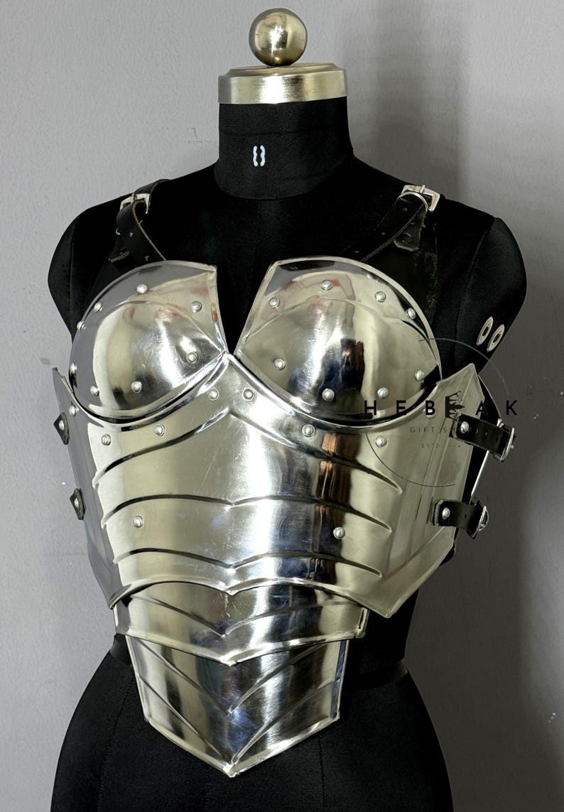 Puede incluir: Un peto plateado pulido con detalles remachados y un dise&ntilde;o esculpido. La armadura presenta un escote curvo y se asegura con correas de cuero negro. El peto se exhibe en un maniqu&iacute; negro.