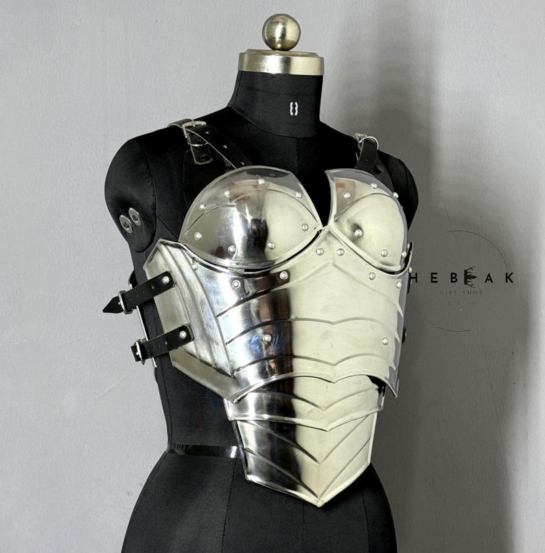 Puede incluir: Un peto plateado pulido con detalles de remaches y correas de cuero, exhibido en un maniqu&iacute; negro. La armadura presenta un dise&ntilde;o contorneado con placas en capas y una superficie reflectante, que evoca un tema medieval o de fantas&iacute;a.