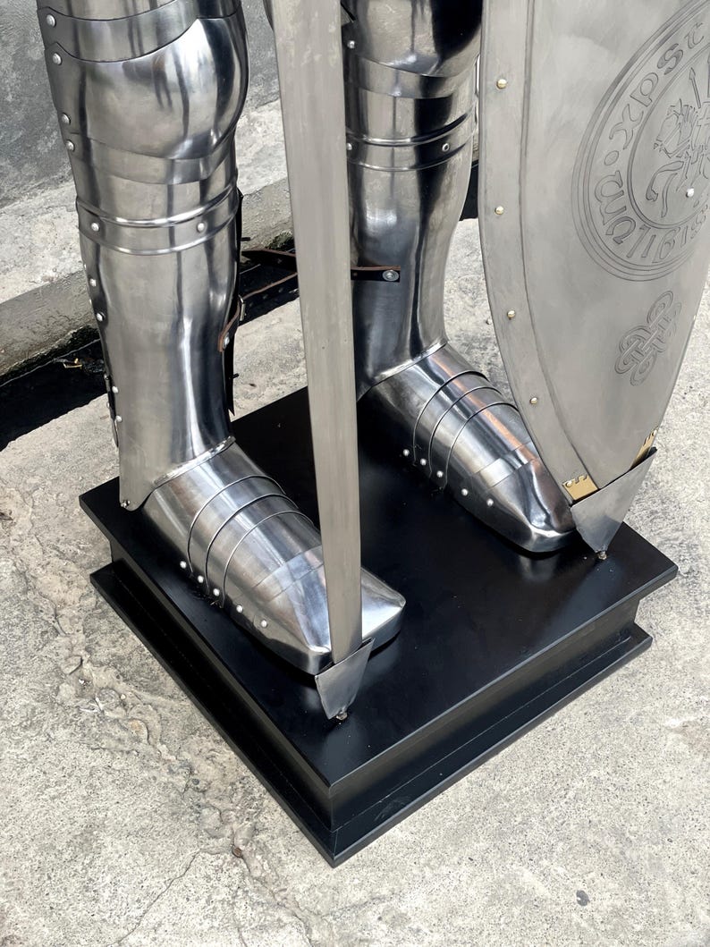 May include: A full suit of silver armor with a sword and shield. The armor is standing on a black wooden base. The shield has a circular design with a crest and the text "32 DSS DUO 11617"