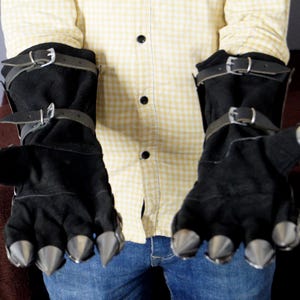 K&ouml;nnte beinhalten: Ein Paar schwarze Lederhandschuhe mit Metallspitzen an den Fingern. Die Handschuhe haben Riemen und Schnallen um die Handgelenke.