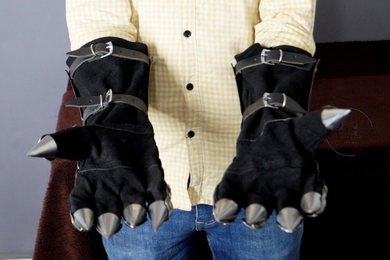 K&ouml;nnte beinhalten: Ein Paar schwarze Lederhandschuhe mit Metallspitzen an den Fingern. Die Handschuhe haben Riemen und Schnallen um die Handgelenke.