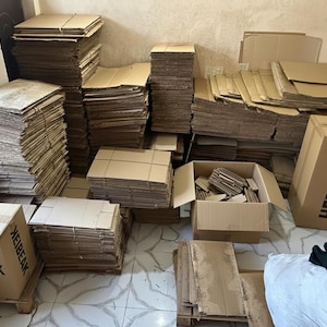 May include: A collection of brown cardboard boxes and stacks of cardboard sheets. Some boxes are assembled, while others are flat. The text "HEBEEAK" is printed on two boxes. The image suggests packaging and shipping supplies.