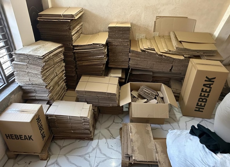 May include: A collection of brown cardboard boxes and stacks of cardboard sheets. Some boxes are assembled, while others are flat. The text "HEBEEAK" is printed on two boxes. The image suggests packaging and shipping supplies.