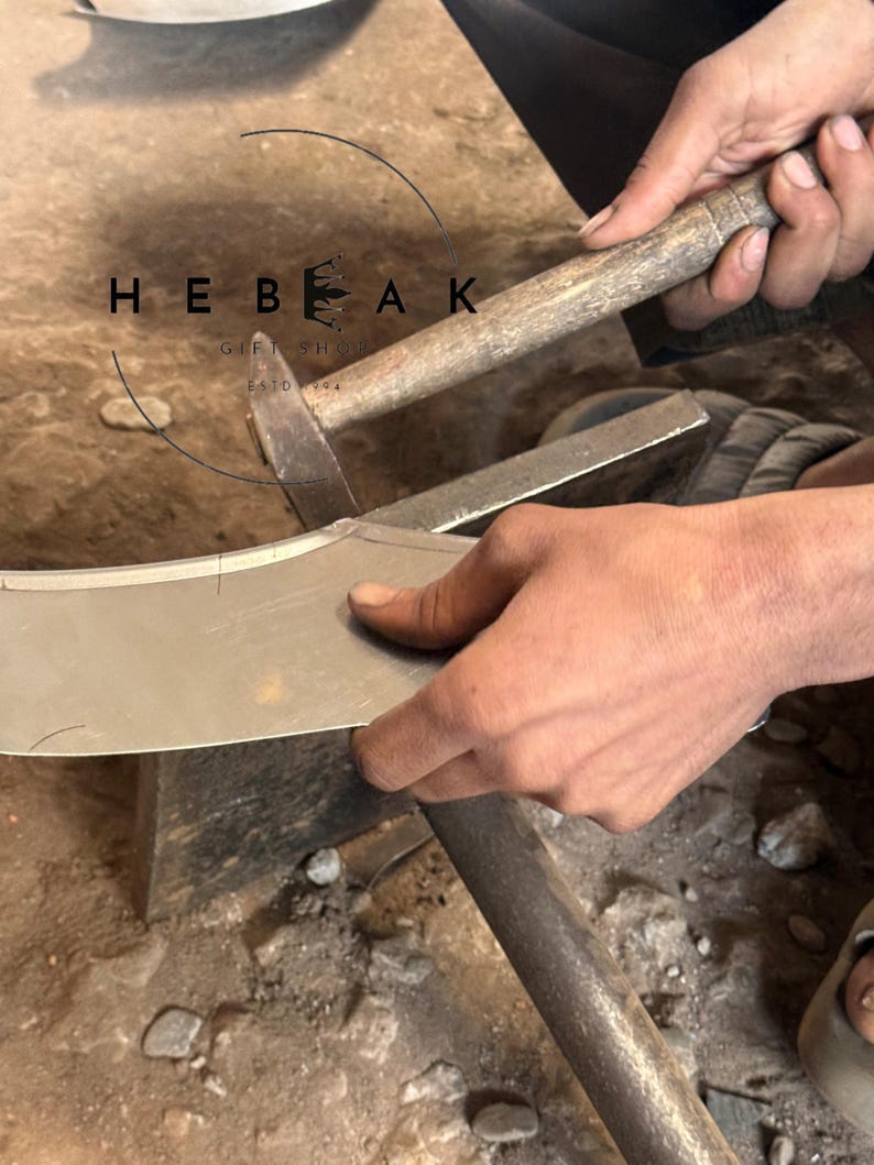 May include: A craftsman uses a hammer and anvil to shape a metal blade. The image shows the process of metalworking, with the text "HEBEAK GIFT SHOP ESTD 1994" in the upper left corner.