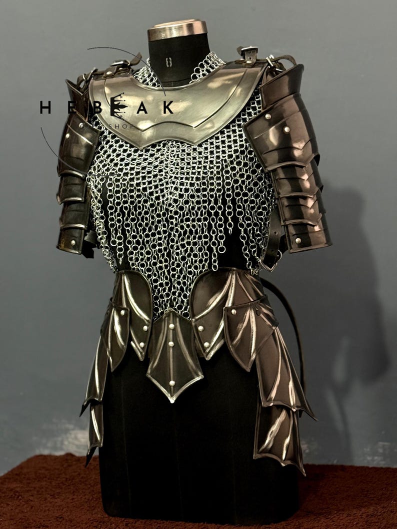 May include: A medieval-style armor set, displayed on a black mannequin. The armor features a silver breastplate, chainmail, and articulated shoulder and arm guards. The lower portion has layered, stylized metal plates. The armor is dark with silver accents.