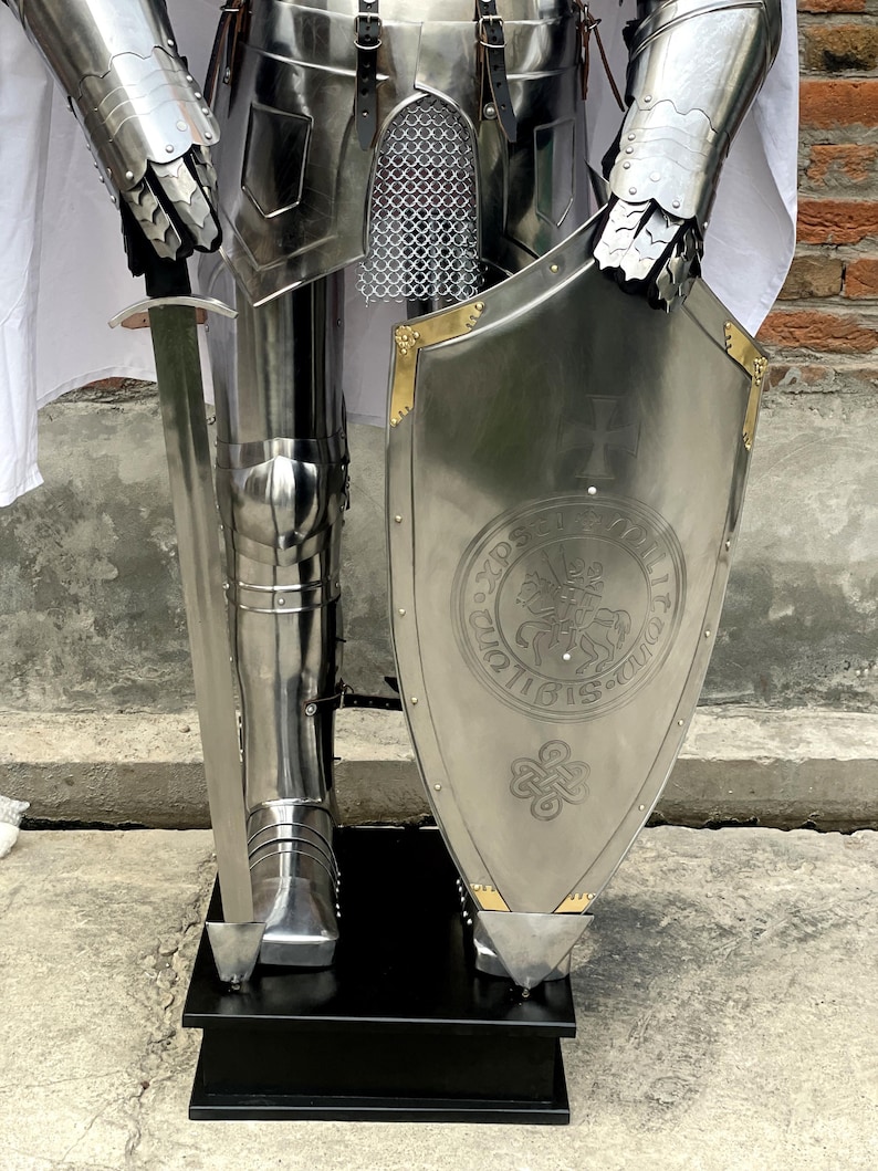 May include: A full suit of silver armor with a sword and shield. The shield has a gold trim and a design of a knight on horseback with a cross.