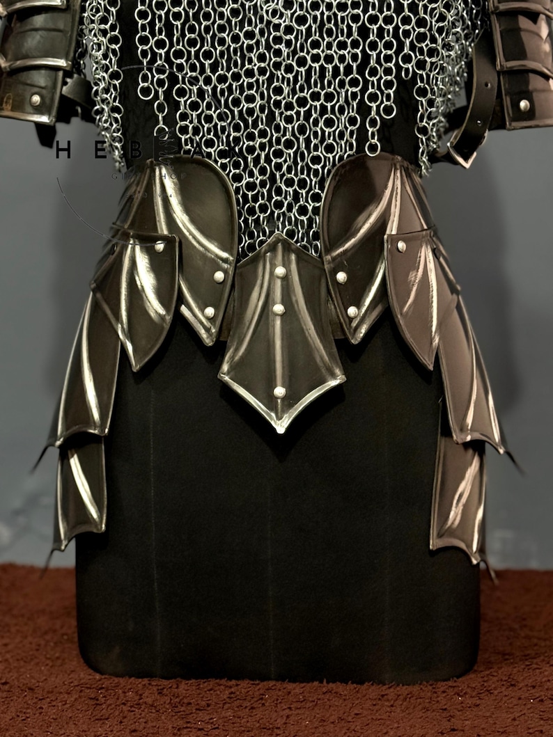 May include: Close-up of a black and silver medieval armor set. The armor features layered leather and metal plates, with chainmail detailing at the top. The design includes decorative elements and rivets, showcasing a detailed craftsmanship.