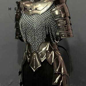 May include: A suit of medieval armor, displayed on a black mannequin. The armor is primarily silver and black, with a chainmail chest piece and layered metal plates. The word "HEAK" is visible on the armor.