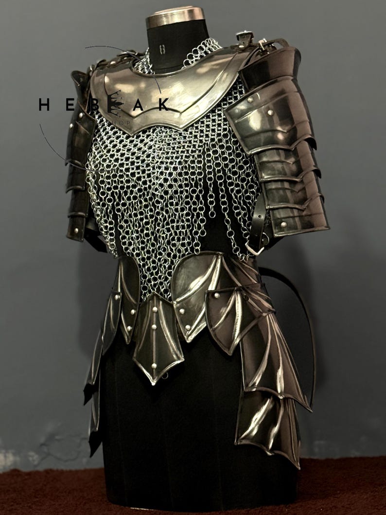 May include: A suit of medieval armor, displayed on a black mannequin. The armor is primarily silver and black, with a chainmail chest piece and layered metal plates. The word "HEAK" is visible on the armor.