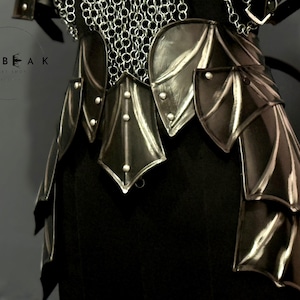 May include: Close-up of a black and silver fantasy armor set. The armor features layered, stylized plates and chainmail detailing. The design includes decorative rivets and a dark, metallic finish, suggesting a medieval or fantasy theme.