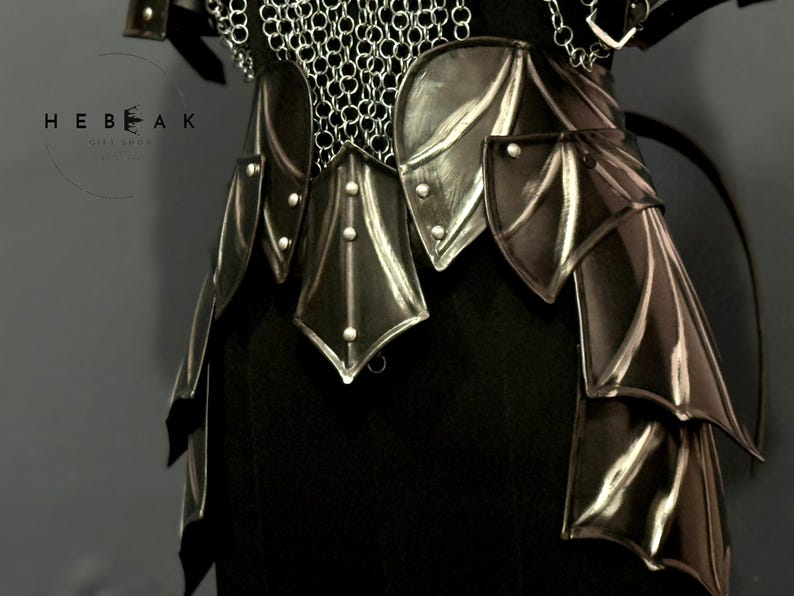 May include: Close-up of a black and silver fantasy armor set. The armor features layered, stylized plates and chainmail detailing. The design includes decorative rivets and a dark, metallic finish, suggesting a medieval or fantasy theme.