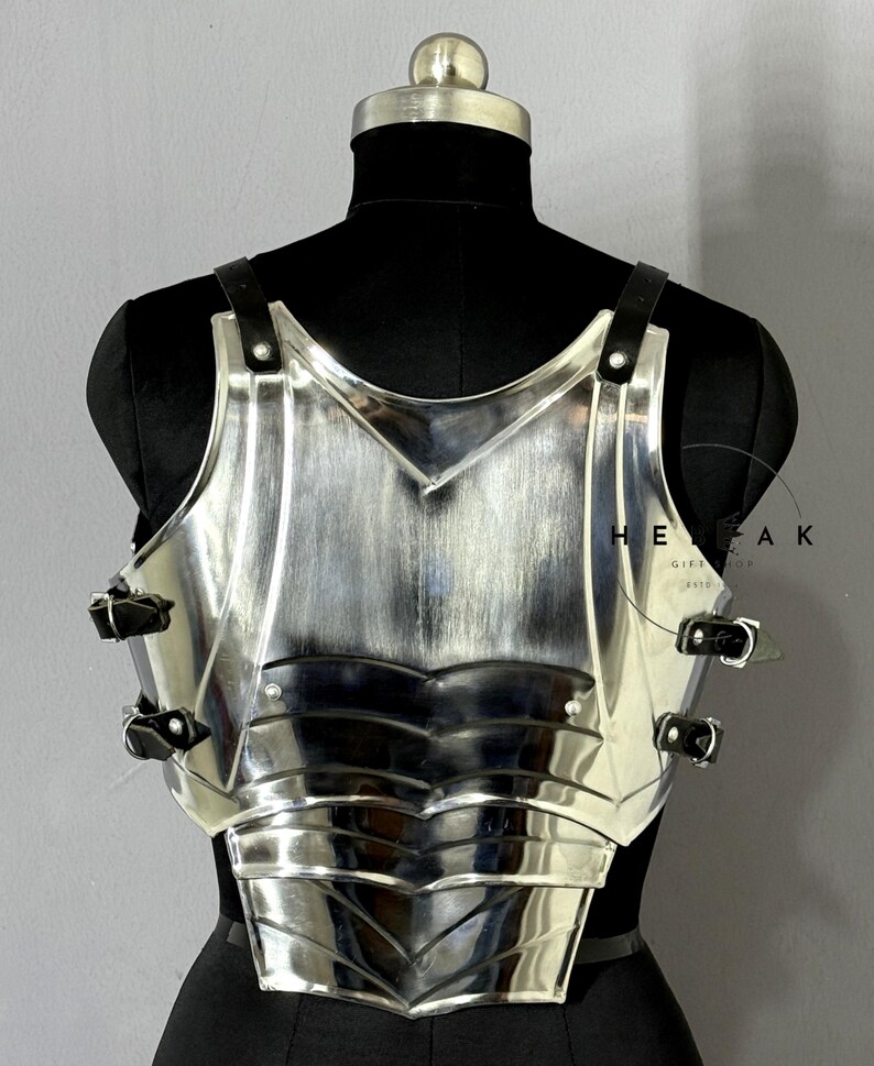 Puede incluir: Una armadura de pecho plateada pulida con correas y hebillas de cuero negro. La armadura se exhibe en un maniqu&iacute; negro. La armadura tiene un dise&ntilde;o en capas con un escote en forma de V y est&aacute; dise&ntilde;ada para proteger el pecho.