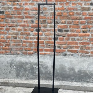 May include: A black metal clothing rack with a square base and two vertical poles. The rack is freestanding and has a horizontal bar at the top.