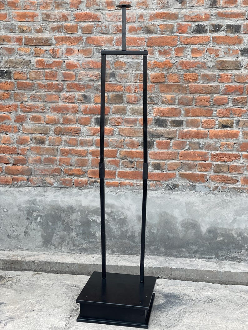 May include: A black metal clothing rack with a square base and two vertical poles. The rack is freestanding and has a horizontal bar at the top.