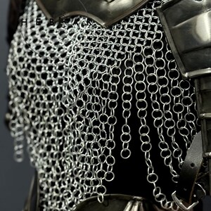 May include: Close-up of a section of medieval armor, showcasing a chainmail shirt and metal shoulder plates. The chainmail is made of small, interlocking silver rings, creating a flexible yet protective layer. Leather straps and buckles are visible, adding to the historical aesthetic.