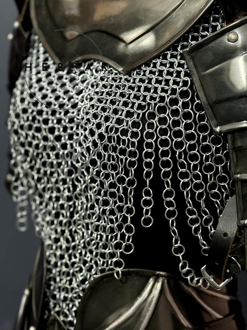May include: Close-up of a section of medieval armor, showcasing a chainmail shirt and metal shoulder plates. The chainmail is made of small, interlocking silver rings, creating a flexible yet protective layer. Leather straps and buckles are visible, adding to the historical aesthetic.