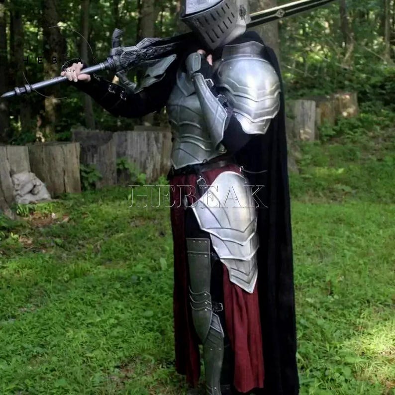 May include: A person wearing silver armor with a black cape and holding a sword. The armor has a detailed design and is made of metal. The person is standing in a forest setting.
