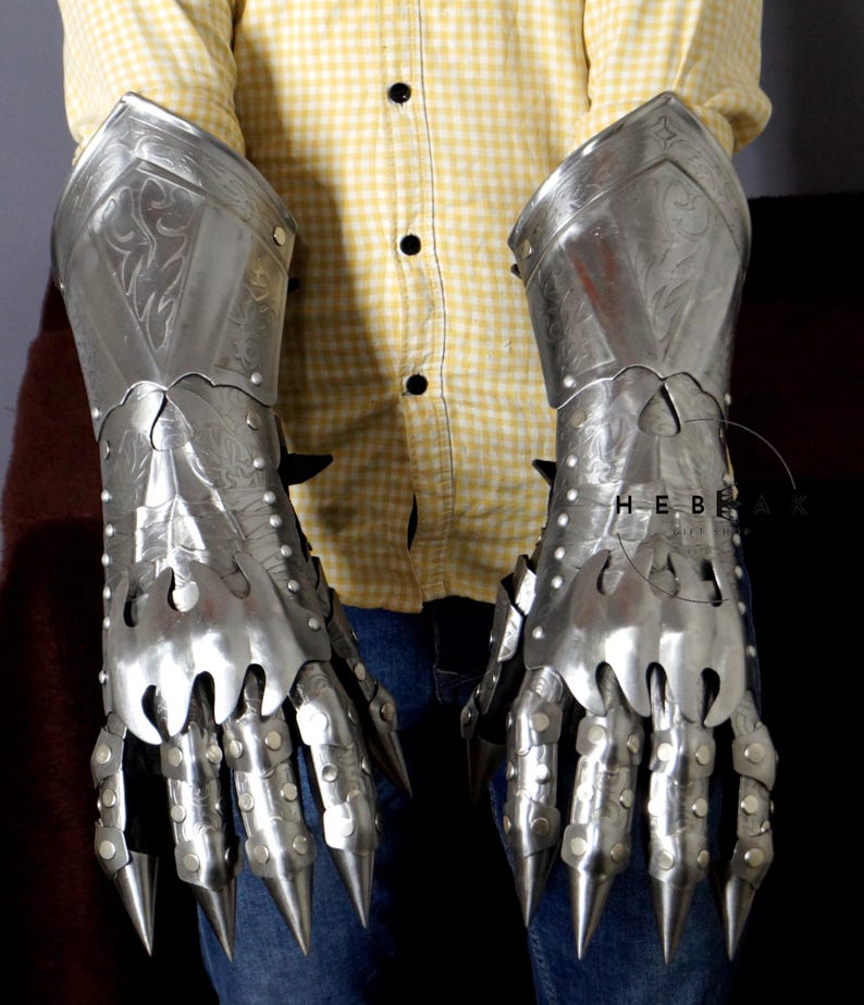 K&ouml;nnte beinhalten: Ein Paar silberne Metallhandschuhe mit Fingerklauen und dekorativen Gravuren. Die Handschuhe werden von einer Person getragen, aber der Fokus liegt auf den Handschuhen selbst.