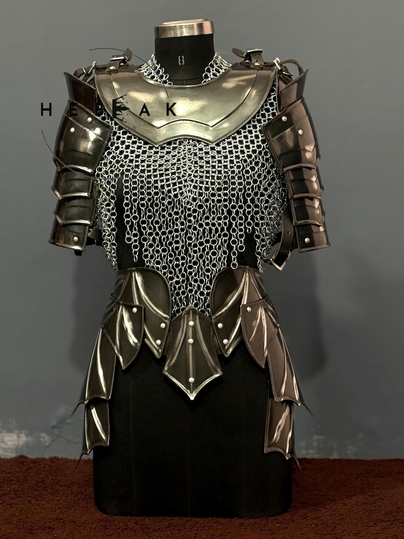 May include: A suit of medieval armor, displayed on a mannequin. The armor is primarily silver and black, with a chainmail shirt and articulated plates. The design includes shoulder pauldrons, a gorget, and a skirt of layered plates. The word "HEAK" is visible on the left side.