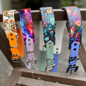 May include: A collection of colorful dog collars with unique designs. The collars feature vibrant patterns including butterflies, abstract art, floral arrangements, and tropical birds. Each collar has a different colored buckle and strap, with orange, purple, green, and blue options.