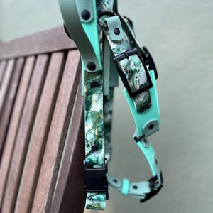 May include: A dog harness with a marbled green and gold pattern, accented with solid mint green straps and black hardware. The harness is made of a durable material and features adjustable buckles for a secure fit.