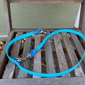 Könnte beinhalten: Eine leuchtend blaue Hundeleine mit silberfarbenen Metallverschlüssen und Nieten. Die Leine besteht aus einem flexiblen, wasserdichten Material und ist auf einem Holzstuhl geschlungen. Die Leine ist für Tierhalter konzipiert.