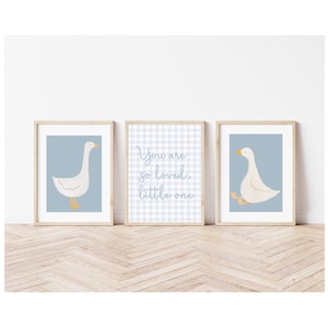 May include: Three framed prints with a blue background. The center print has a white and blue gingham pattern with the text "You are so loved. little one". The prints on either side feature a white goose with orange feet on a blue background.