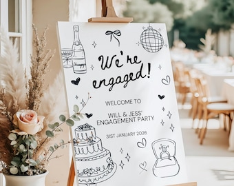 May include: White sign on a wooden easel with the text "We're engaged!" and illustrations of a champagne bottle, cake, and ring. The sign welcomes guests to Will & Jess' Engagement Party on January 31st, 2026.