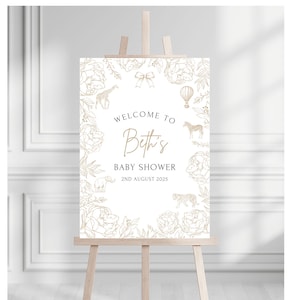 May include: A baby shower welcome sign on a wooden easel. The sign is white with gold floral and animal illustrations. Text reads "Welcome to Beth's Baby Shower 2nd August 2025".