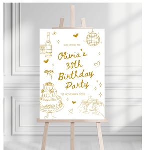 May include: A gold-colored sign on an easel, announcing "Olivia's 30th Birthday Party" with illustrations of champagne, a cake, and disco ball. The date "1st November 2025" is also displayed. The sign is on a wooden easel.