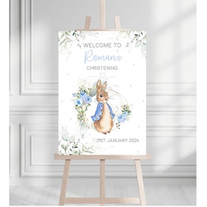 Op de afbeelding: Welkom op het doopbord van Roman met een aquarel-illustratie van Peter Rabbit in een blauw jasje, omringd door blauwe bloemen en groen. De datum is 21 januari 2024.