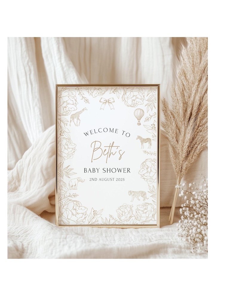 May include: A framed baby shower sign with a gold border. The sign reads "Welcome to Beth's Baby Shower 2nd August 2025". The sign is decorated with floral and animal illustrations in a gold color.
