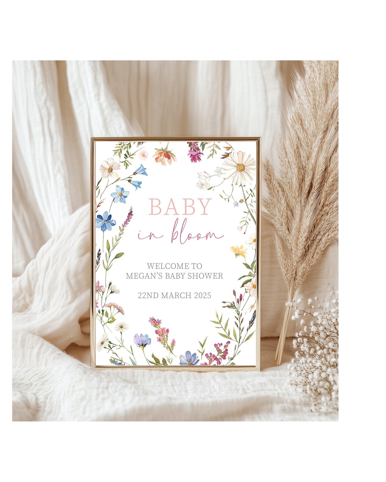 May include: A white sign with a floral border and the text "Baby in bloom" in pink lettering. The sign also includes the text "Welcome to Megan's Baby Shower" and "22nd March 2025".