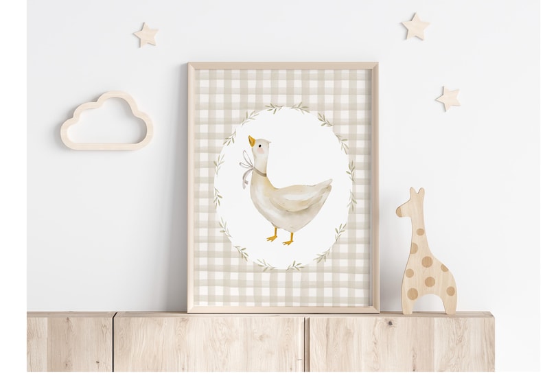 May include: A framed print with a beige and white gingham pattern. The print features a watercolor illustration of a white goose with a yellow beak and feet, surrounded by a wreath of green leaves. The goose is standing on a white background.