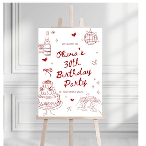 May include: A white sign on an easel with red illustrations and text. The sign reads "Welcome to Olivia's 30th Birthday Party" with a cake, champagne bottle, disco ball, and glasses. The date "1st November 2025" is also included.