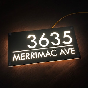 May include: A black illuminated house number sign with white lettering. The number 3635 and the street name Merrimac Ave are displayed on the sign.