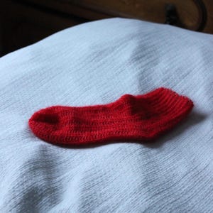 May include: A red knitted sock on a light blue fabric background.