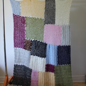 Könnte beinhalten: Eine rechteckige Häkeldecke mit einem Patchwork-Design aus verschiedenfarbigen Garnquadraten. Die Farben umfassen Hellblau, Gelb, Dunkelgrau, Creme, Magenta, Olivgrün, Rosa, Hellgrau, Schwarz und Dunkelbraun in einem lockeren Maschenbild.