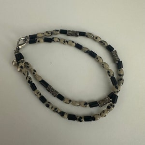 Puede incluir: Un brazalete de doble cadena con cuentas de color blanco y negro con manchas y detalles plateados.