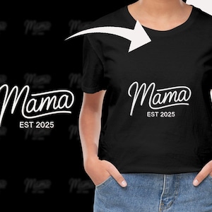 Op de afbeelding: Zwart T-shirt met het woord "Mama" in witte scriptletter, met "EST 2025" eronder. Het shirt heeft een ronde hals.