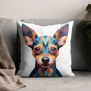 Op de afbeelding: Een decoratief sierkussen met een geometrisch ontwerp van een hondengezicht. Het gezicht van de hond is weergegeven in een mozaïek van blauwe, oranje en bruine vormen op een witte achtergrond. Het kussen ligt op een grijze bank.