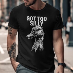 Op de afbeelding: Zwart t-shirt met de tekst "GOT TOO SILLY" in verweerde witte letters boven een gedetailleerde grijswaarden illustratie van een eendenkop. Het t-shirt heeft korte mouwen.