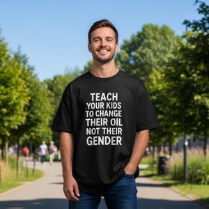 Może przedstawiać: Czarny t-shirt z białym napisem: "TEACH YOUR KIDS TO CHANGE THEIR OIL NOT THEIR GENDER." Koszulka ma okrągły dekolt. Zdjęcie zrobiono na zewnątrz w słoneczny dzień.