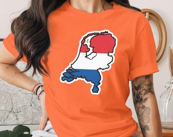 Puede incluir: Camiseta naranja con un gráfico del mapa de los Países Bajos en rojo, blanco y azul, delineado en negro. La camiseta tiene mangas cortas.