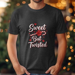 Op de afbeelding: Donkergrijs T-shirt met de tekst "Sweet But Twisted" in witte letters en een zuurstokontwerp. Rode harten en een strik accentueren het ontwerp. Ronde hals.