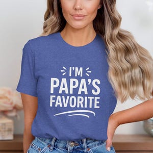 Op de afbeelding: Blauw t-shirt met de witte tekst "I'M PAPA'S FAVORITE". Het shirt heeft een ronde hals en korte mouwen. De tekst staat in het midden op de voorkant van het shirt.