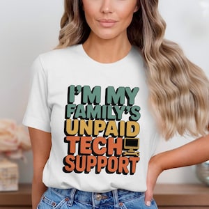 Op de afbeelding: Wit T-shirt met de tekst "I'M MY FAMILY'S UNPAID TECH SUPPORT" in teal, geel, oranje en zwart. Het ontwerp bevat een computerpictogram. Het shirt wordt door een persoon gedragen.