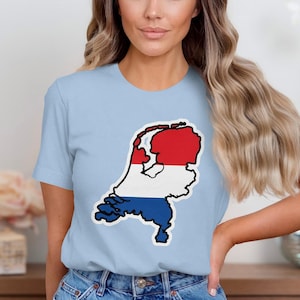 Op de afbeelding: Een lichtblauw T-shirt met een afbeelding van Nederland in de kleuren van de Nederlandse vlag: rood, wit en blauw. De afbeelding is een kaartomtrek van het land. Het shirt is gemaakt van zacht materiaal.
