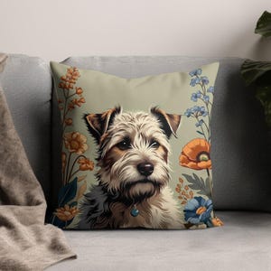Op de afbeelding: Vierkant kussen met een illustratie van een terriër-achtige hond met een bloemenrand. De hond heeft bruin en wit haar, met een blauwe hanger. De bloemen zijn oranje, blauw en geel op een lichtgroene achtergrond.